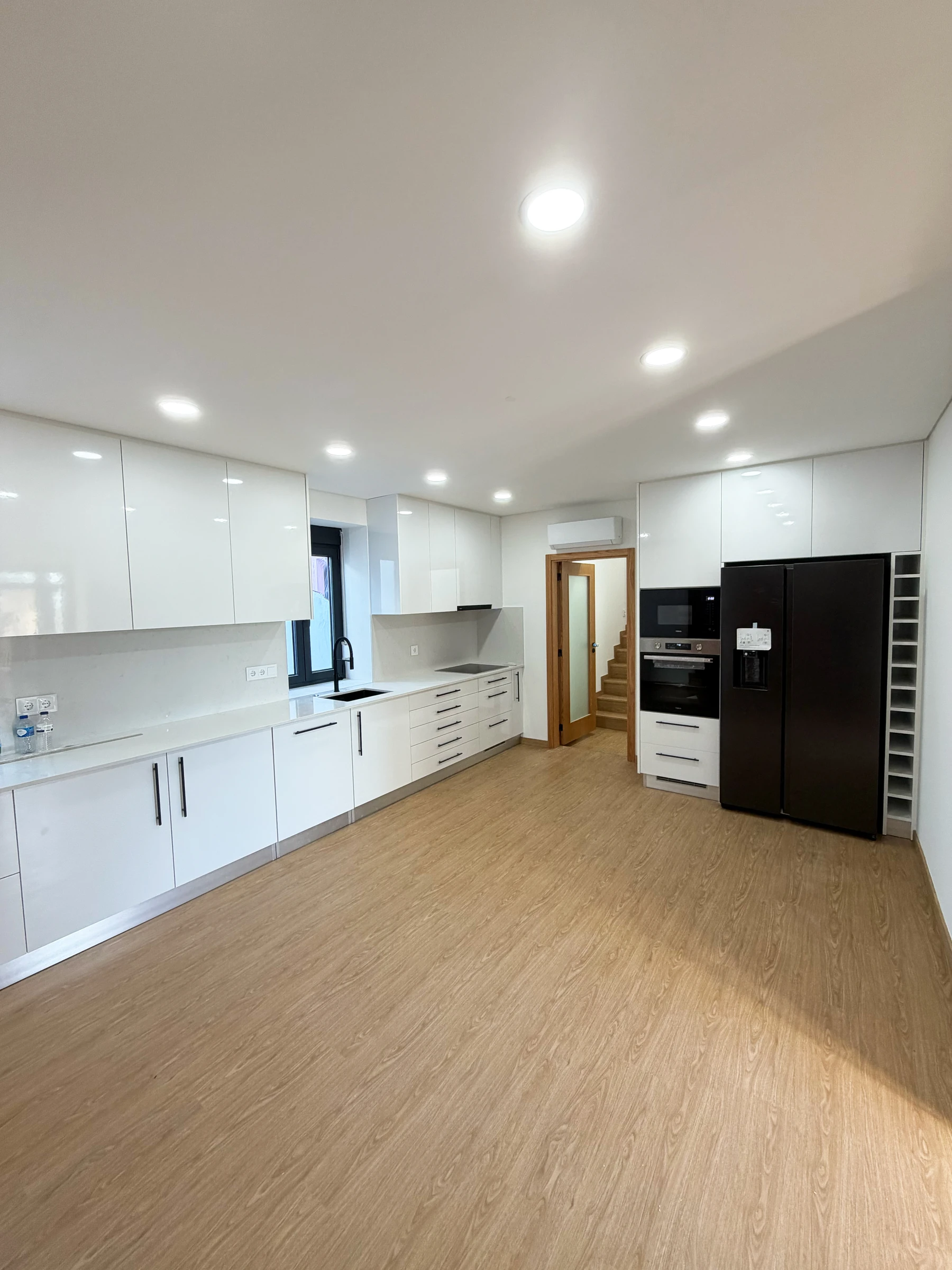 Cozinha moderna em open space em Estarreja, Aveiro, com mobiliário lacado branco, bancadas em quartzo e pavimento vinílico efeito madeira — remodelação VPObras