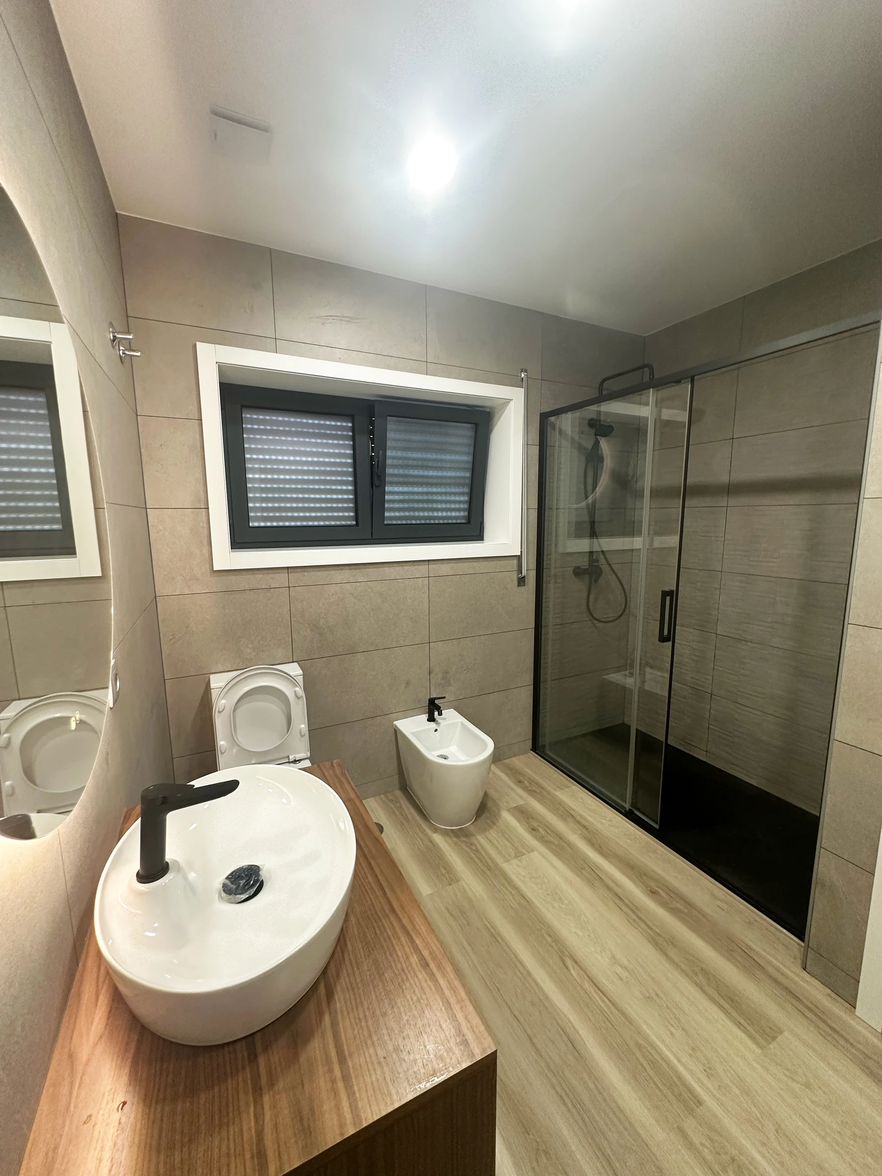 Casa de banho moderna em Estarreja, Aveiro, com duche de base preta, resguardo em vidro temperado e pavimento vinílico efeito madeira — remodelação VPObras